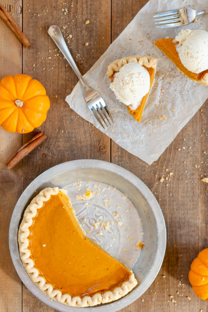 homemade cinnamon ice cream on top of two slices of pumpkin pie and a pumpkin pie in a dish with slices cut out