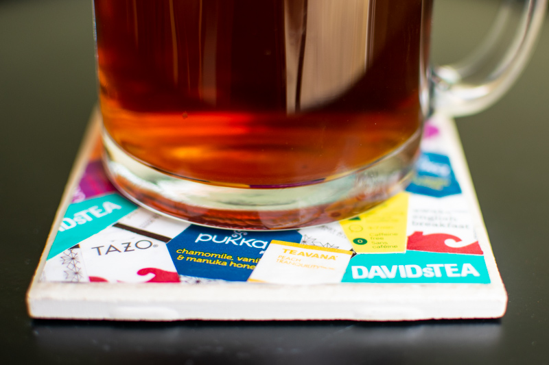 cup of tea on top of a diy coaster tile covered in a collage of tea bag tags