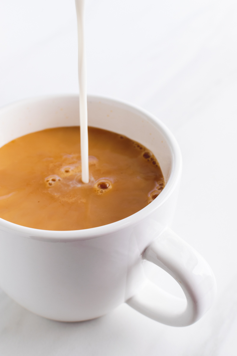 stream of milk being poured into black tea to make milk tea