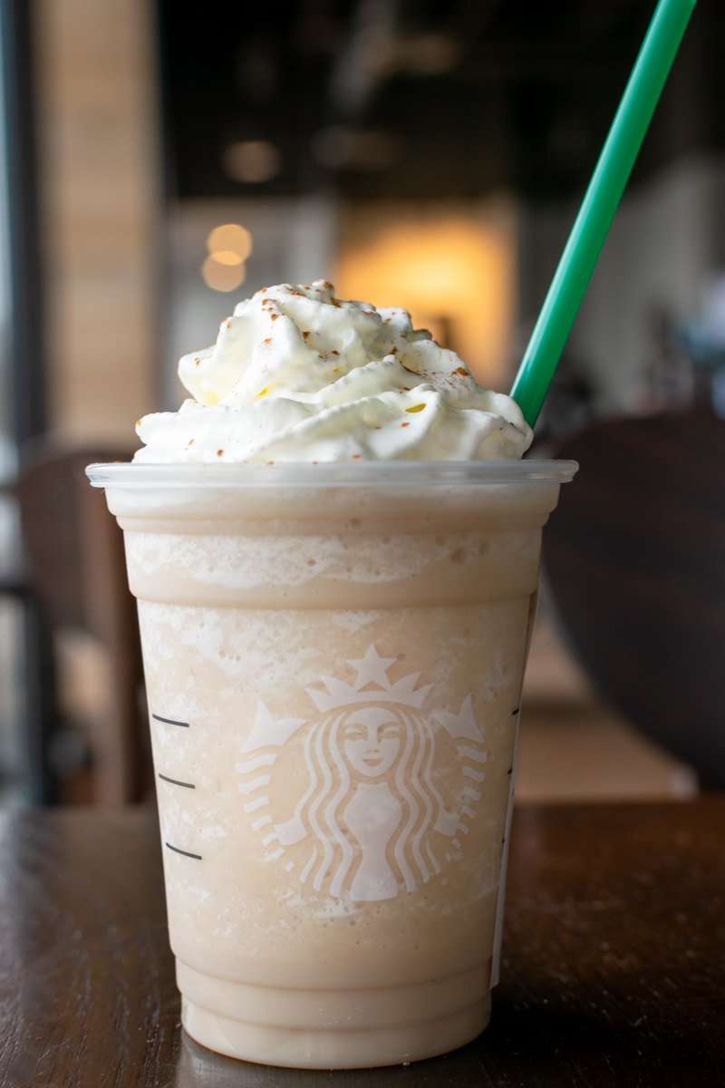 Starbucks chai frappuccino with whipped cream and cinnamon in a cup with a green straw