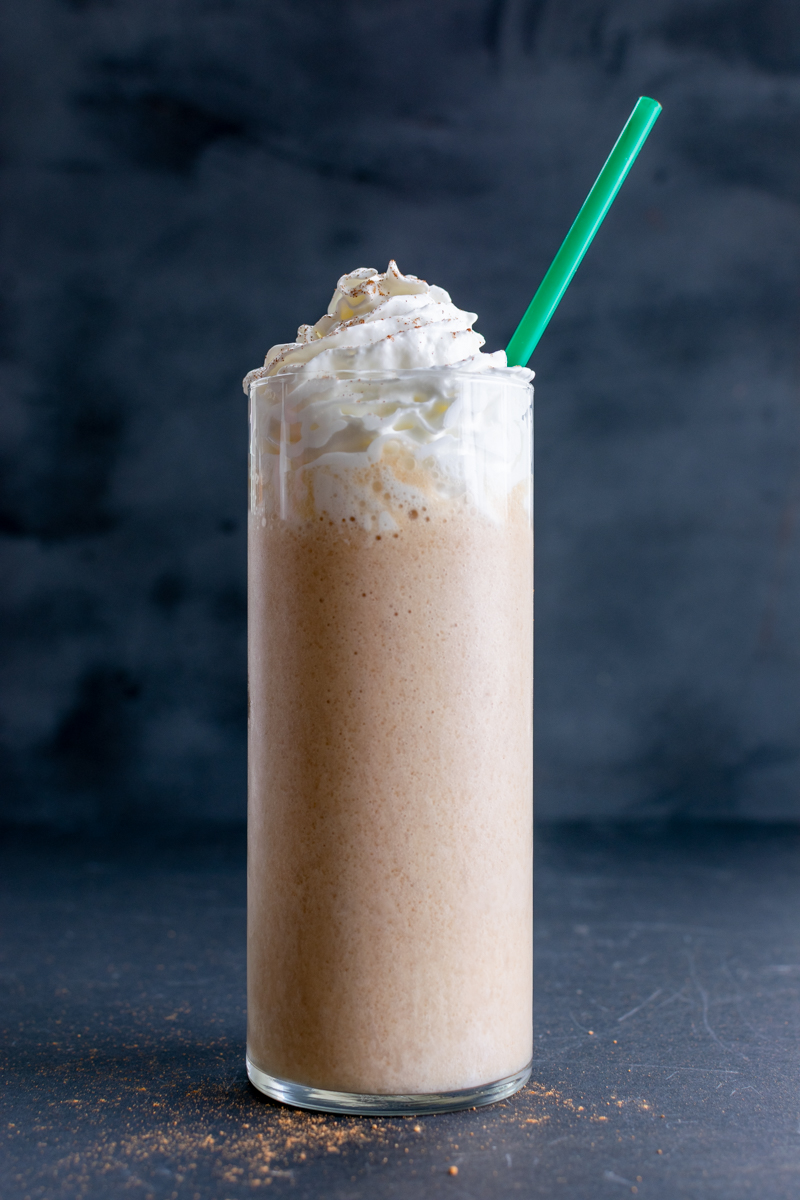 starbucks copycat chai frappuccino recipe in a glass with whipped cream and a green straw