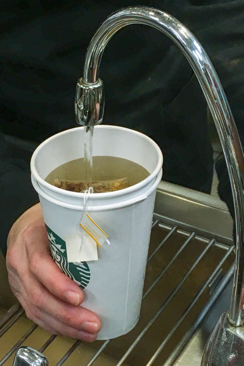 water being poured in a starbucks cup with teavana tea bags
