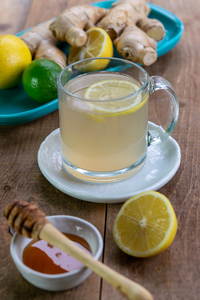 cup adrak chai with lemon, ginger root and bowl of honey