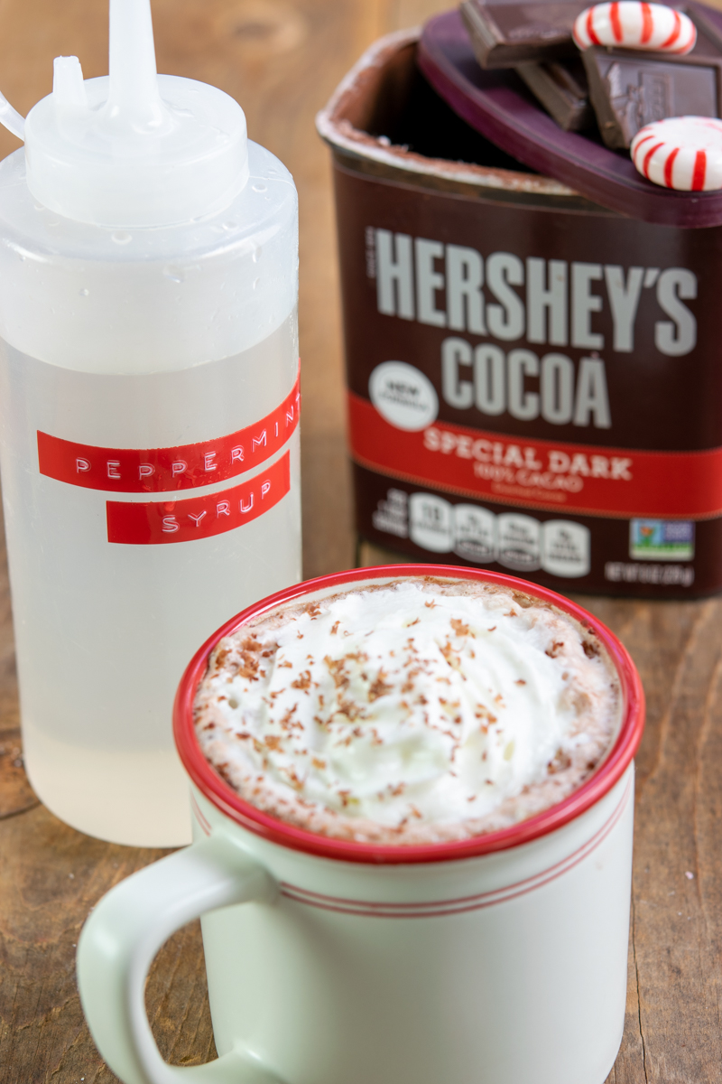 bottle of homemade peppermint syrup, hershey's cocoa and cup of hot cocoa