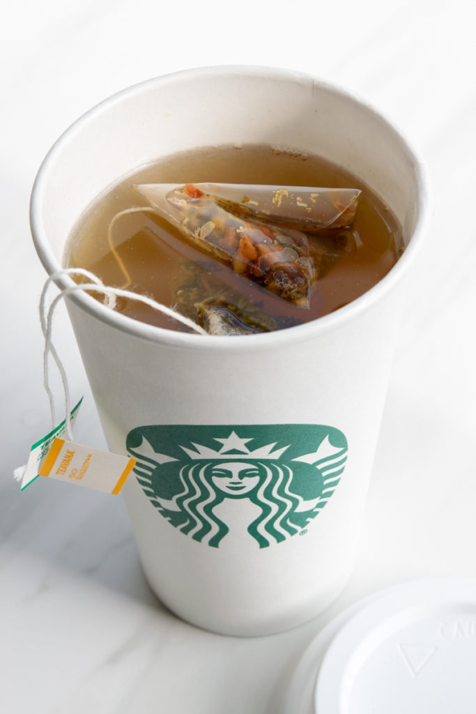 Starbucks cup full of hot tea with jade citrus mint tea bag and peach tranquility tea bags steeping.
