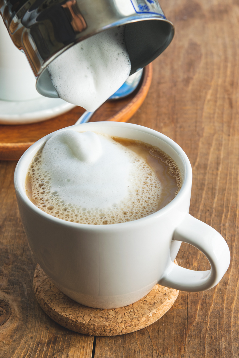 pouring frothed milk from electric milk frother into tea latte