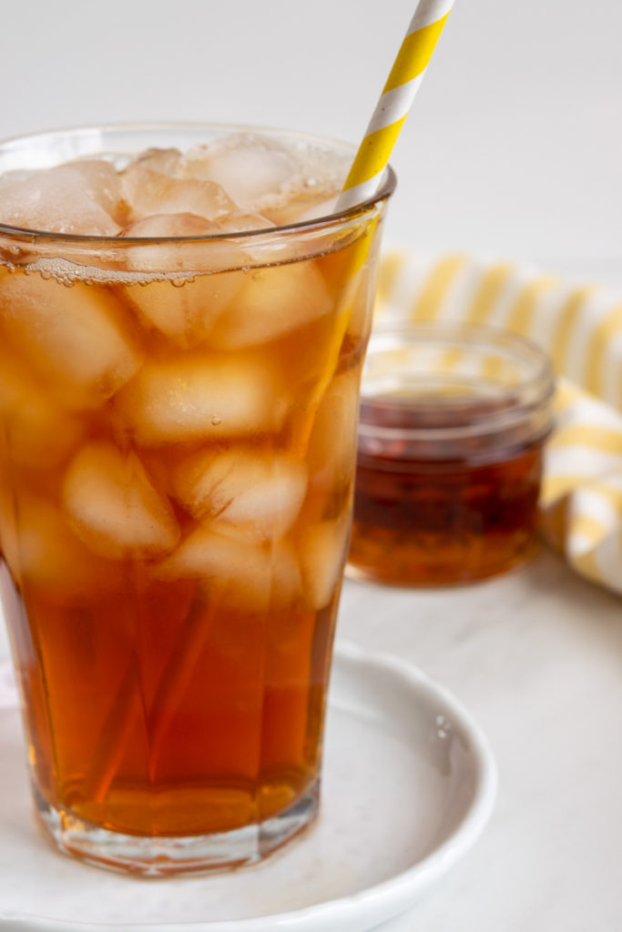 glass of iced tea with straw and bottle of homemade liquid cane sugar syrup