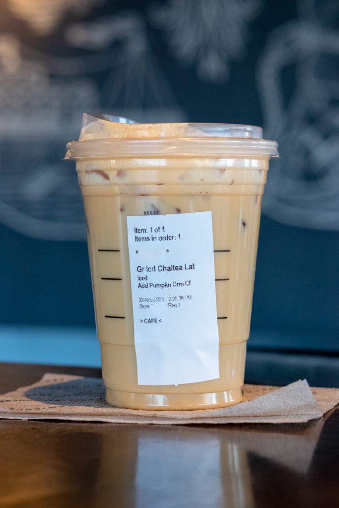 A grande size iced chai tea latte with pumpkin cold foam on top and label on the side of cup showing custom drink order.