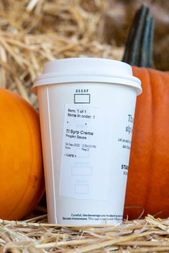 A tall size pumpkin spice steamer in a Starbucks hot cup in front of pumpkins.