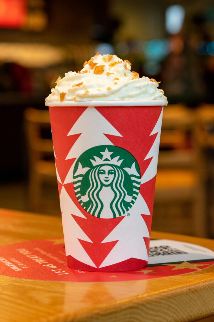 Caramel Brulée Crème in a red holiday cup sitting on a table inside Starbucks with the sugary caramel brulée topping shining in the light.