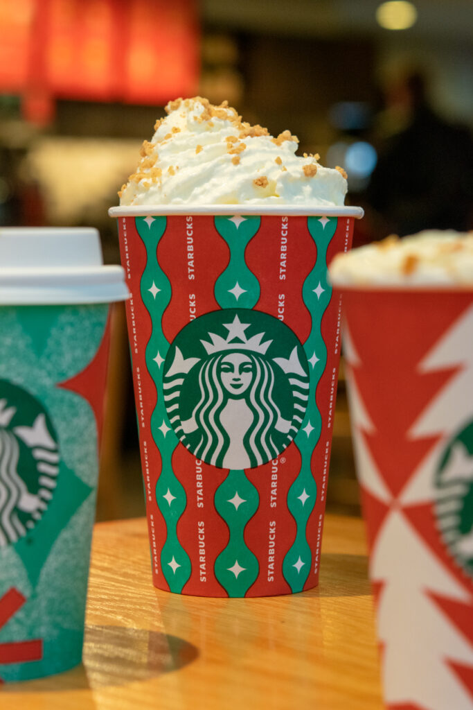 A Starbucks chestnut praline creme sitting in between two other Starbucks holiday drinks.