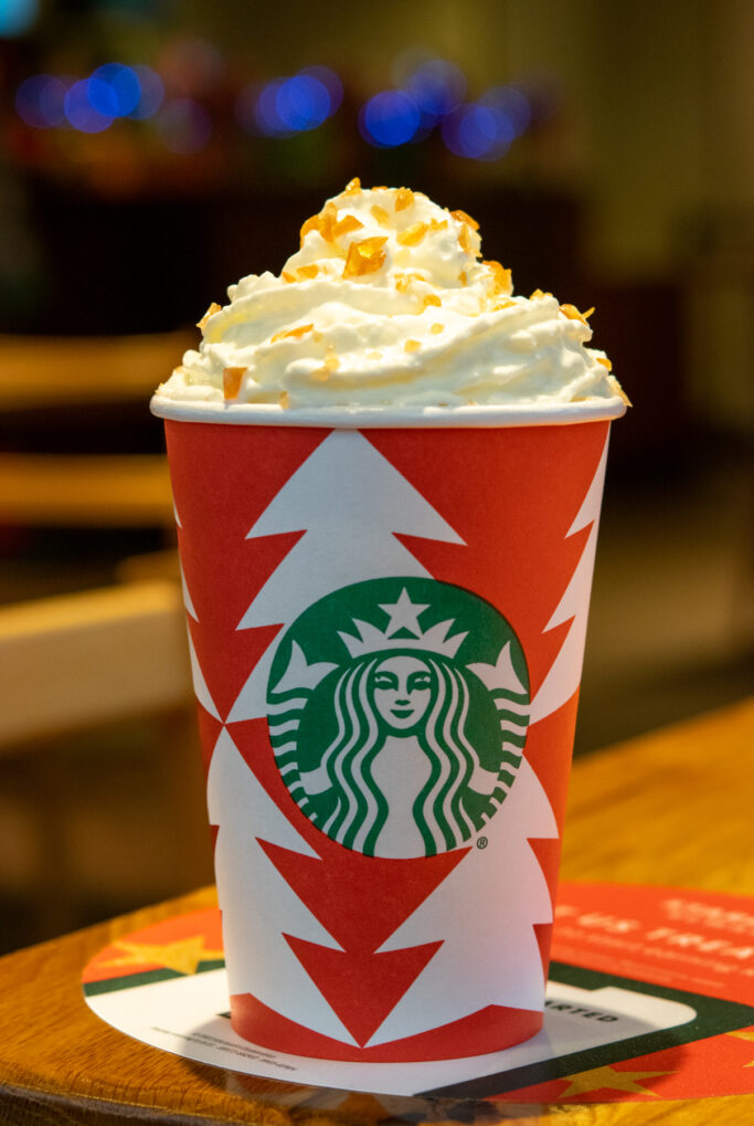 A tall size caramel brulee creme steamer in a red holiday cup.