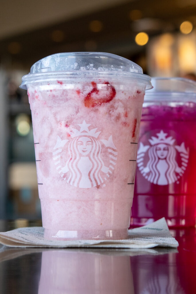 A Starbucks Pink Drink on a table with a Mango Dragonfruit Refresher behind it.