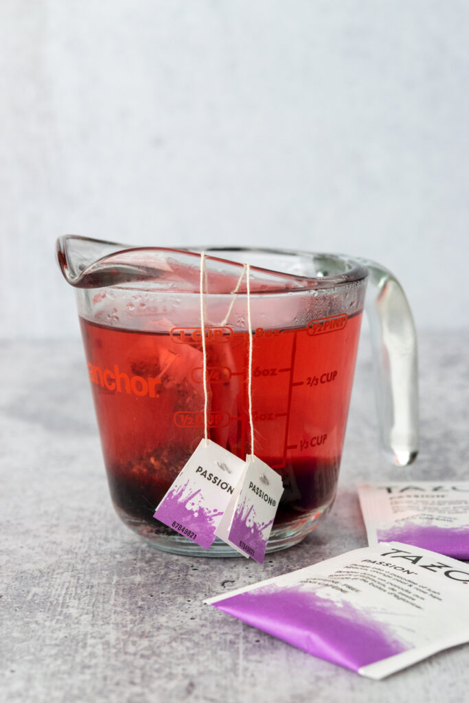 Two Tazo passion tea bags steeping in a cup with hot water added.