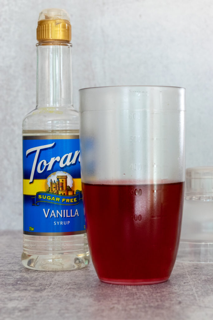 Bottle of sugar-free vanilla syrup next to drink shaker being used to make an at-home keto pink drink.