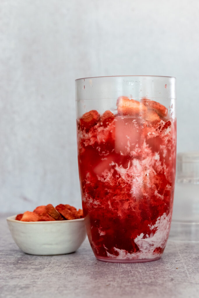 Small bowl containing freeze-dried strawberries next to a shaker containing keto pink drink ingredients.