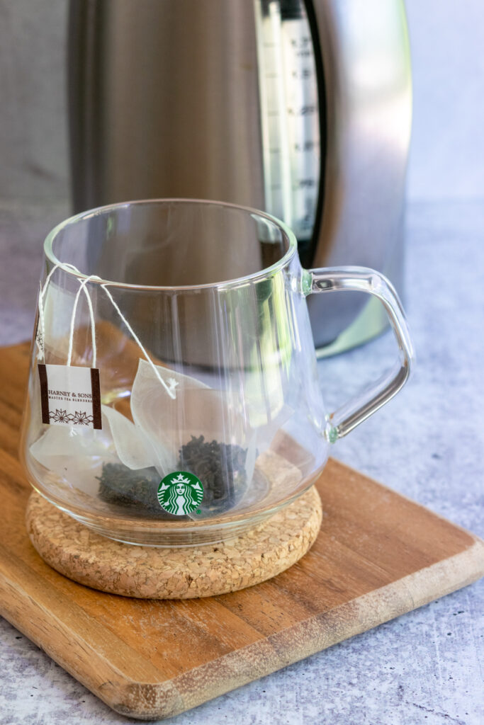 Two earl grey tea bags in a Starbucks mug with tea kettle in the background.