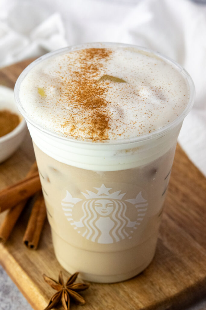 Homemade iced chai tea latte in a Starbucks cup with a thick layer of sweet cream cold foam on top that's sprinkled with cinnamon.