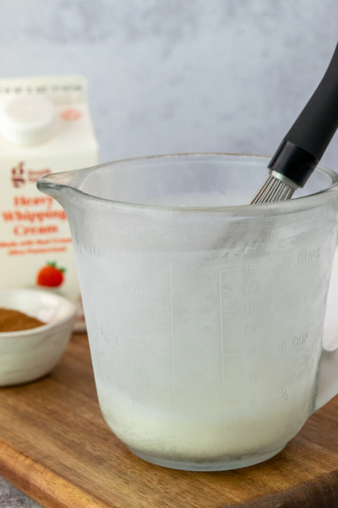 A cold glass measuring cup just out of the freezer that has sweet cream ingredients in it and a whisk.