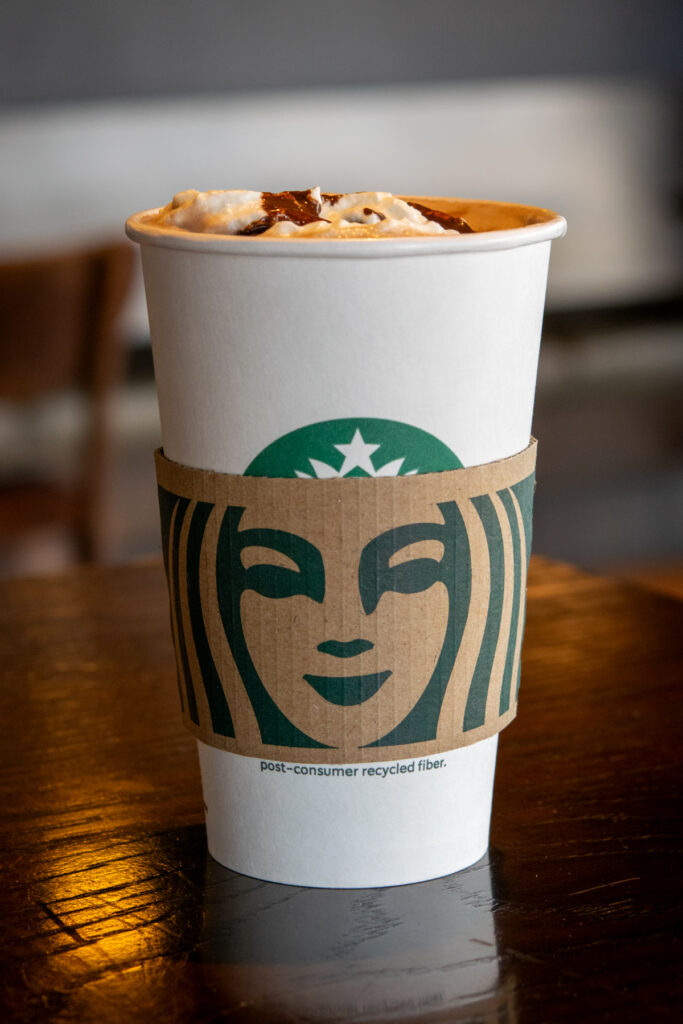 The lid of a Starbucks hot chocolate showing the whipped cream and chocolate sauce melting into the hot drink.