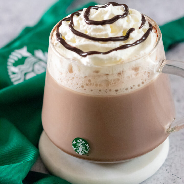 Starbucks Hot Chocolate made at home in a Starbucks mug next to a green Starbucks apron.