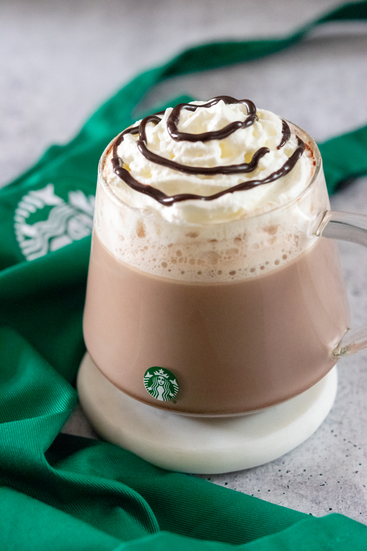 Starbucks Hot Chocolate made at home in a Starbucks mug next to a green Starbucks apron.