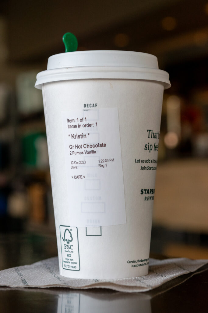 A grande Starbucks Hot Chocolate in a hot cup with the order sticker showing that it has 2 pumps of vanilla added in.