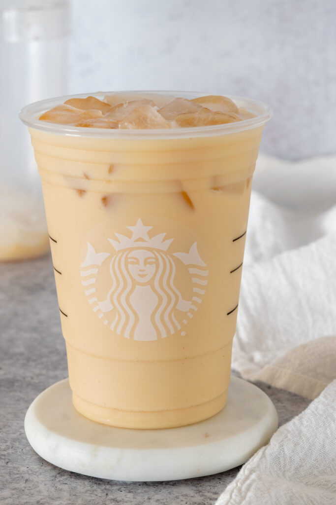 A copycat Starbucks Iced London Fog Tea Latte in a Starbucks cup and the drink shaker it was poured out of in the background.