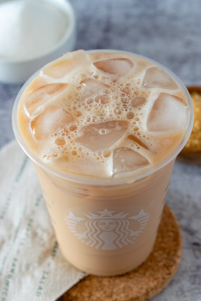 A copycat Starbucks Iced English Breakfast tea latte just poured into a Starbucks cup with the foamy bubbles and ice showing on top.