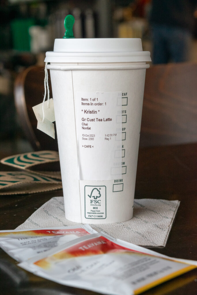 The order sticker on the side of a Starbucks cup showing a grande custom tea latte with chai tea bags and non-fat milk.