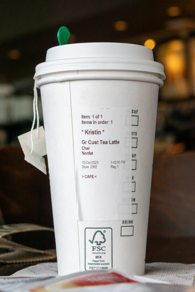 A Starbucks cup with chai tea bags hanging out, showing the order sticker for a custom tea latte with chai and non-fat milk.