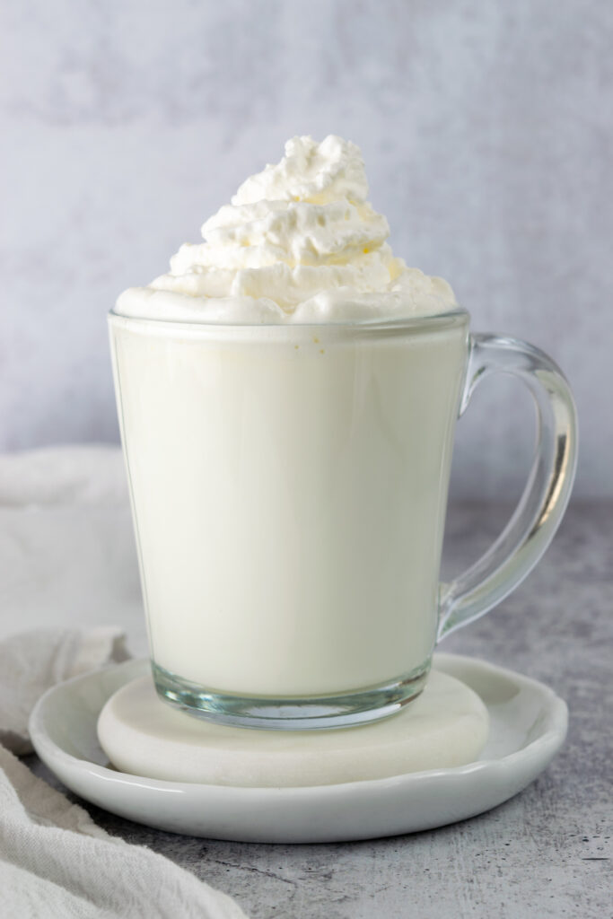 A vanilla steamer in a glass mug topped with whipped cream, showcasing this all-white, creamy beverage.