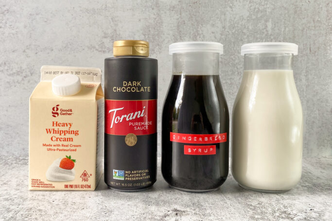Carton of heavy whipping cream, bottle of dark chocolate sauce, jar of homemade gingerbread syrup and bottle of milk.