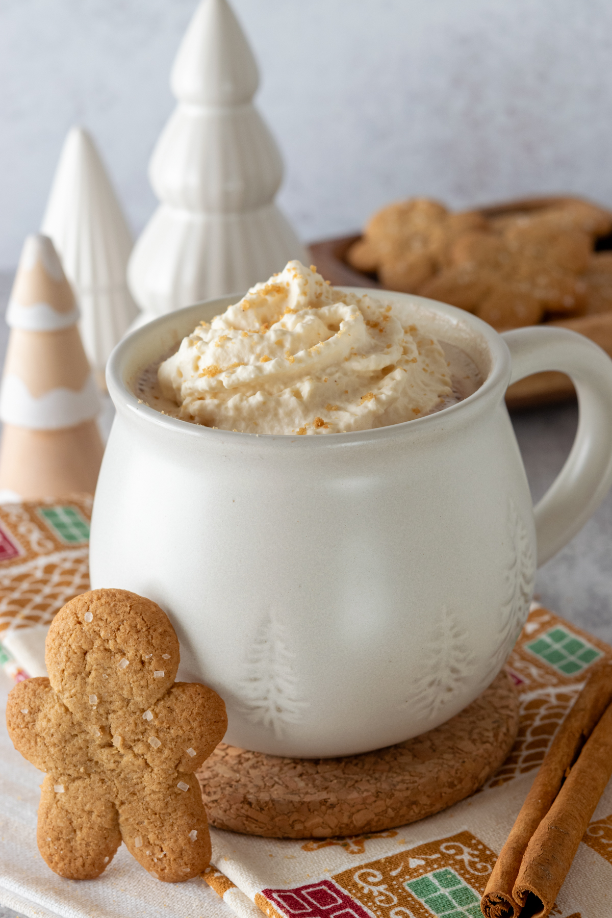 Gingerbread hot chocolate in a winter mug with gingerbread cookies next to it.