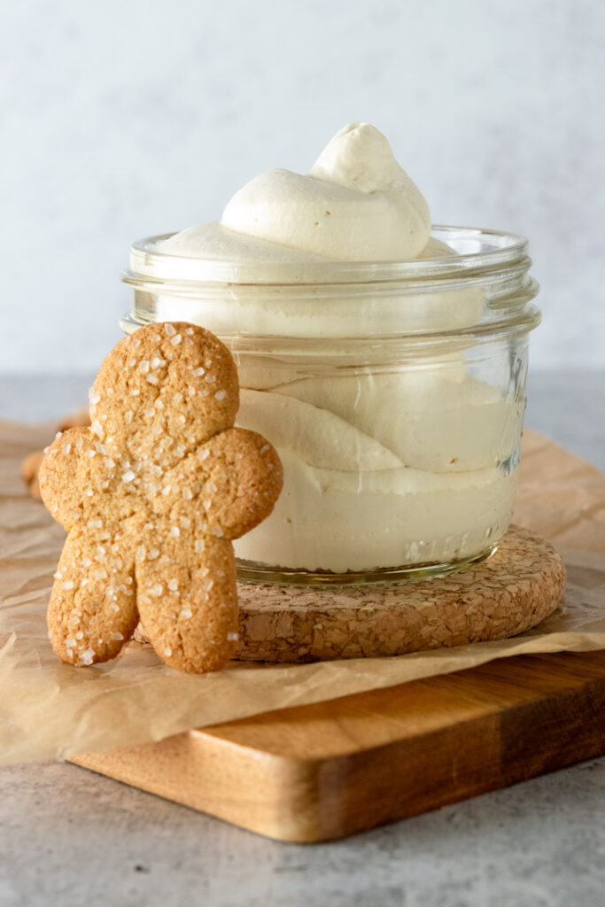 Gingerbread cookie and a glass jar with a dollop of gingerbread whipped cream in it.