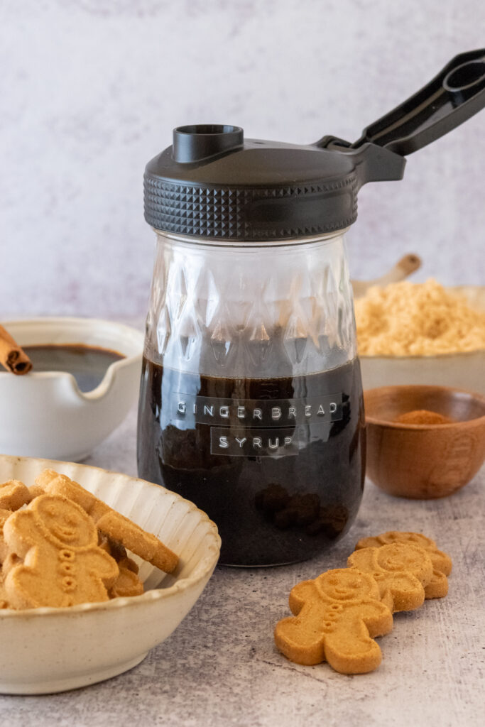 Small bowls of gingerbread cookies, molasses, cinnamon and brown sugar, next to a jar of homemade gingerbread syrup.