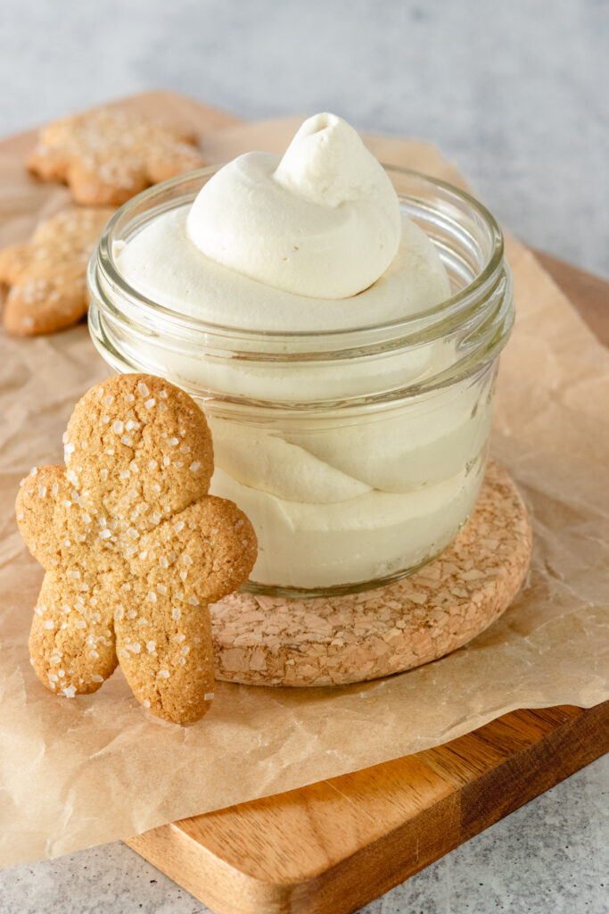 Homemade gingerbread whipped cream in a glass jar with a gingerbread cookie leaning against it.