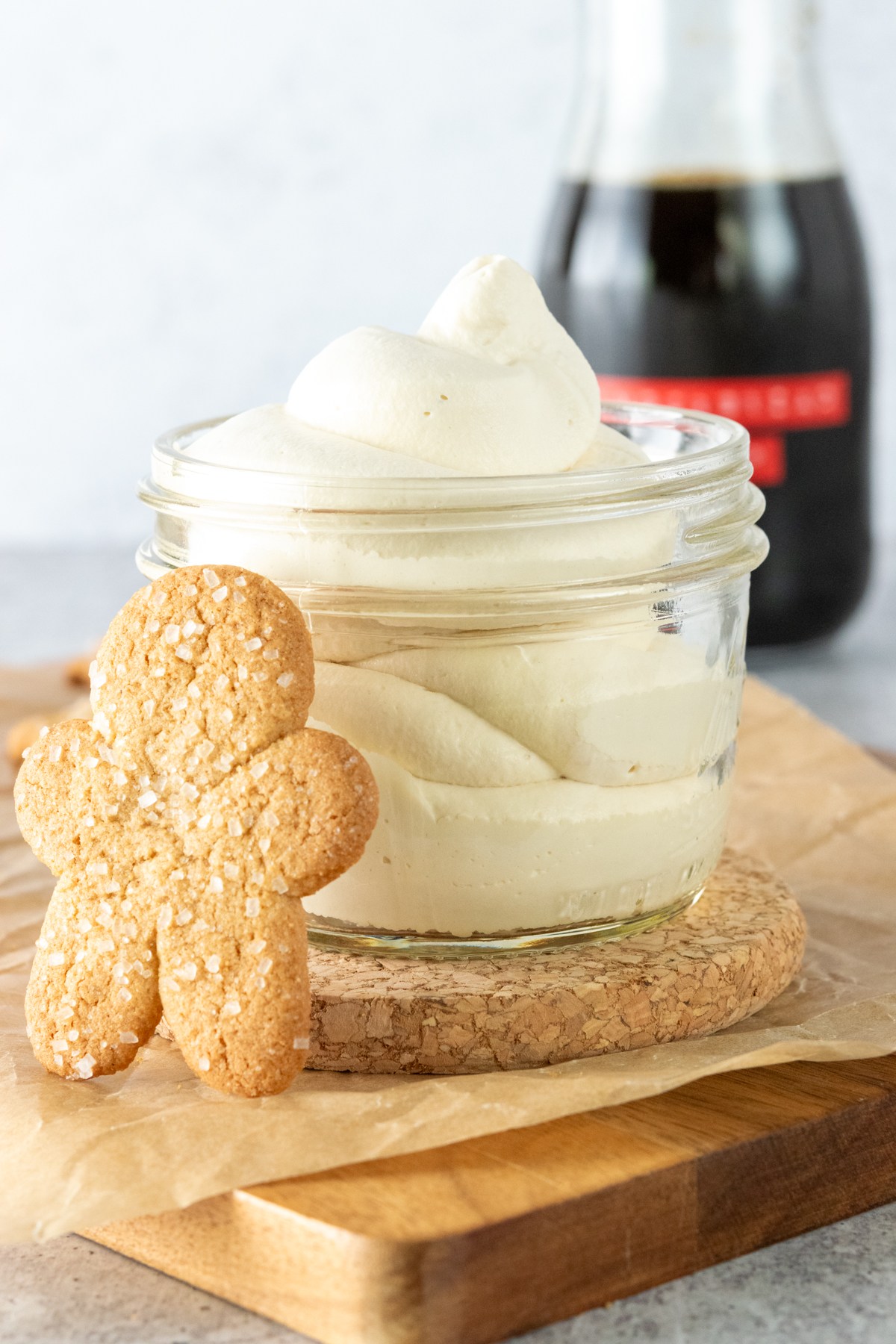 Homemade gingerbread whipped cream in front of a bottle of gingerbread syrup and with a gingerbread cookie leaning against jar of whipped cream.