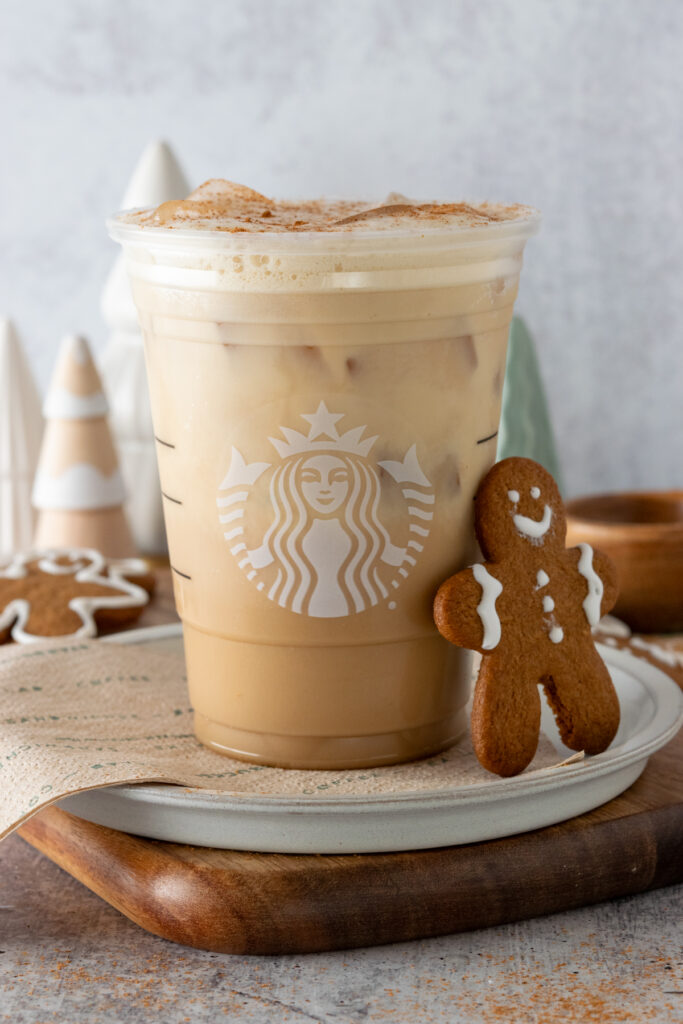 Starbucks Iced Gingerbread Chai Tea Latte made at home in a Starbucks cup with a gingerbread man cookie leaning on cup.