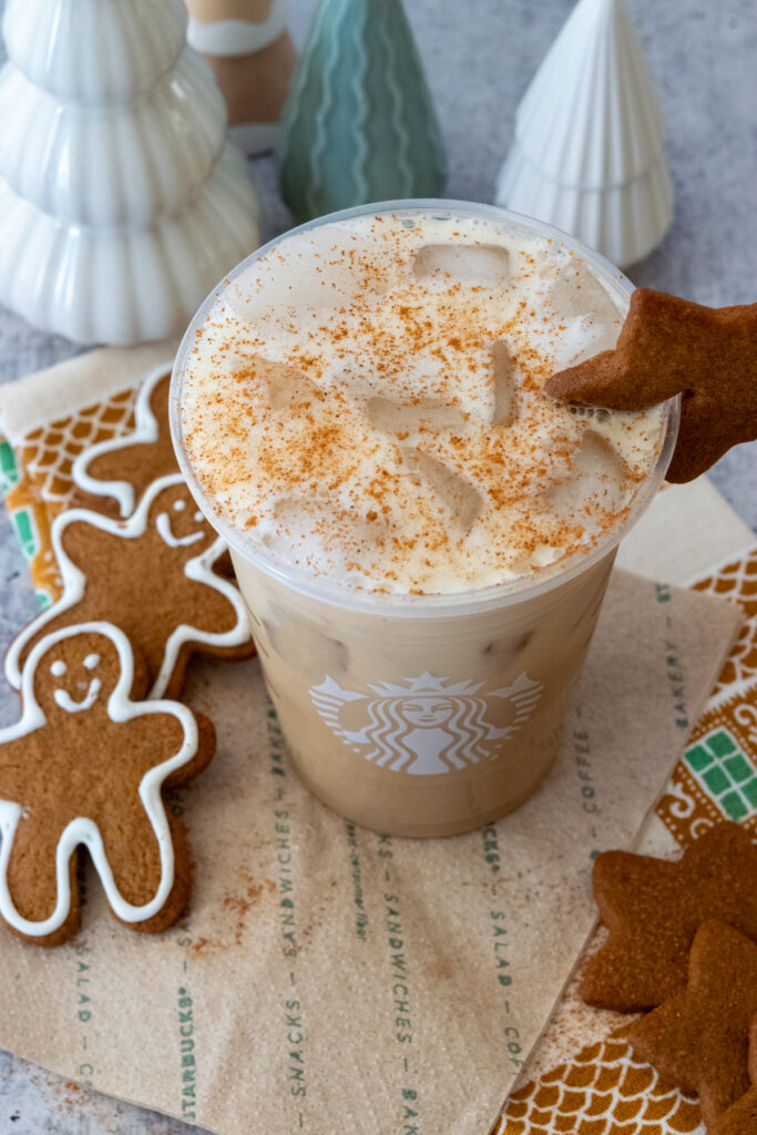 A copycat Starbucks Iced Gingerbread Chai Latte surrounded by gingerbread cookies, showing the creamy gingerbread oat milk and cinnamon topping.