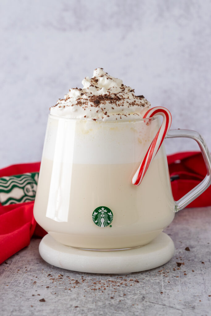 Homemade Starbucks peppermint white hot chocolate in a glass Starbucks mug with a peppermint candy cane on rim of cup.