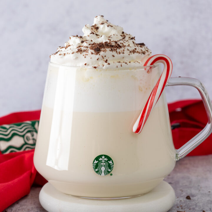 Homemade Starbucks peppermint white hot chocolate in a glass Starbucks mug with a peppermint candy cane on rim of cup.