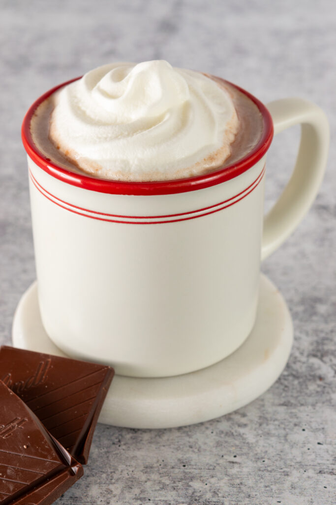 Hot chocolate served in a red and white mug with a topping of whipped cream.