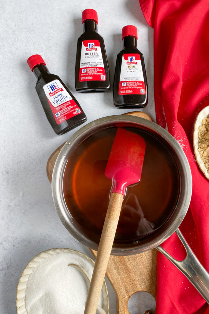 Homemade sugar cookie syrup in a saucepan. There are three bottles of flavored extracts next to the syrup: vanilla, butter and almond.
