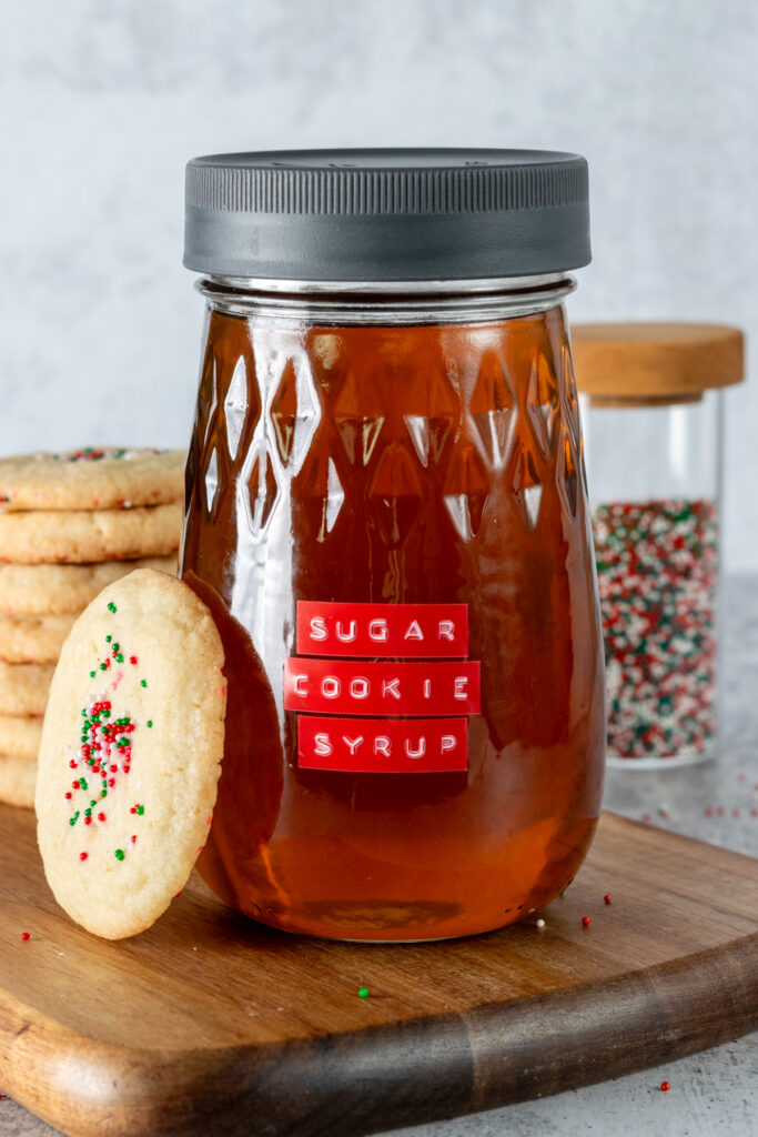 Homemade sugar cookie coffee syrup in a glass bottle which is next to a plate of sugar cookies.