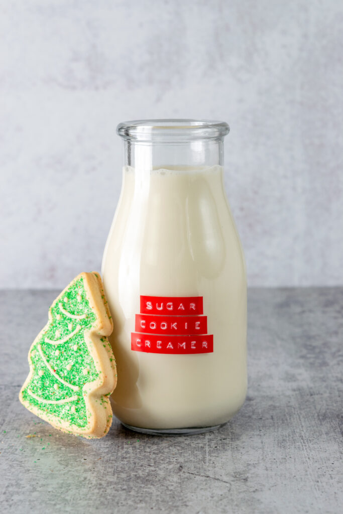 Christmas tree-shaped sugar cookie leaning against a bottle of homemade sugar cookie coffee creamer.