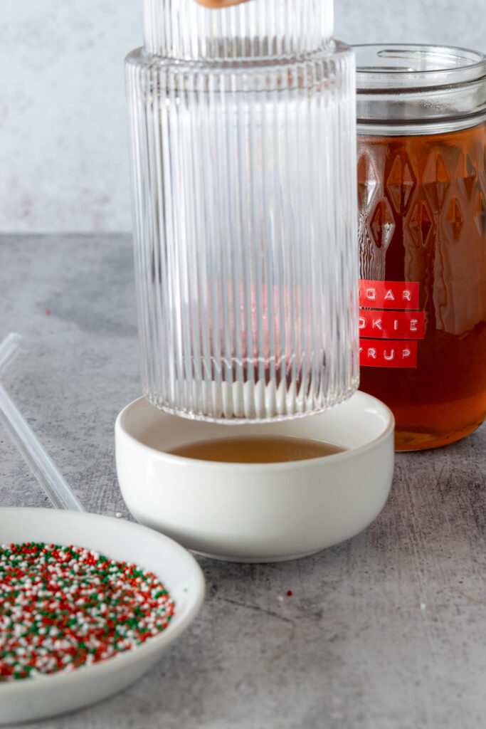 Dipping the rim of a glass into sugar cookie syrup.