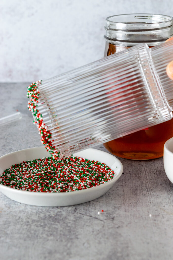 Rolling the rim of a glass that has syrup on it in holiday sprinkles.