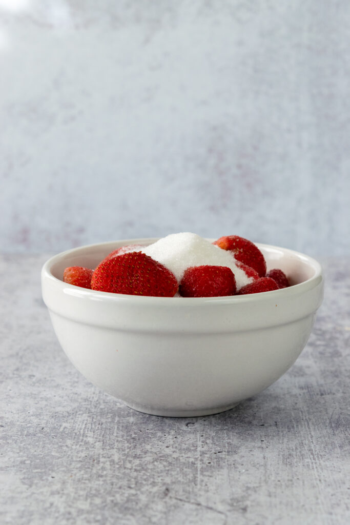 Sugar poured on top of strawberries in a bowl.
