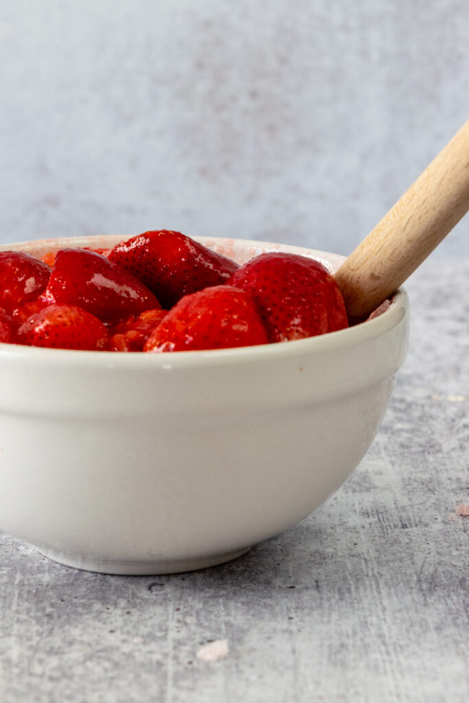 The sugar being stirred into strawberries which are getting juicy.